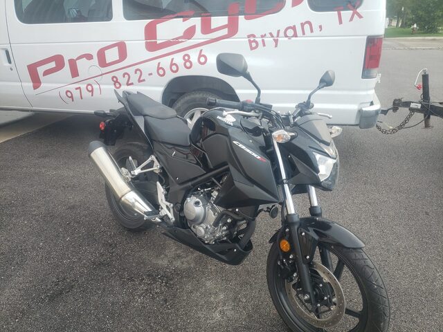 A Honda CB300F parked beside the lettered Pro Cycle shop van
